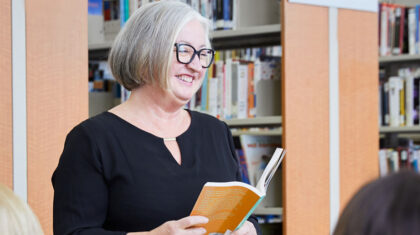 Une dame debout dans une bibliothèque avec un livre dans ses mains