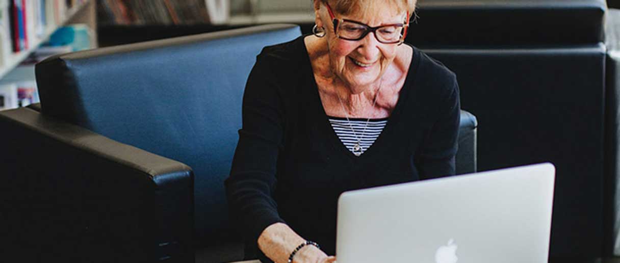 Une ainée dans une bibliothèque devant son ordinateur portable