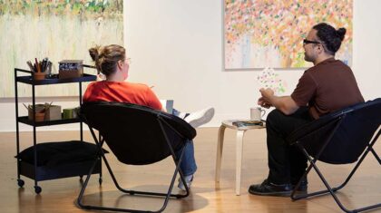 2 personnes assises discutent en regardant des toiles sur le mur
