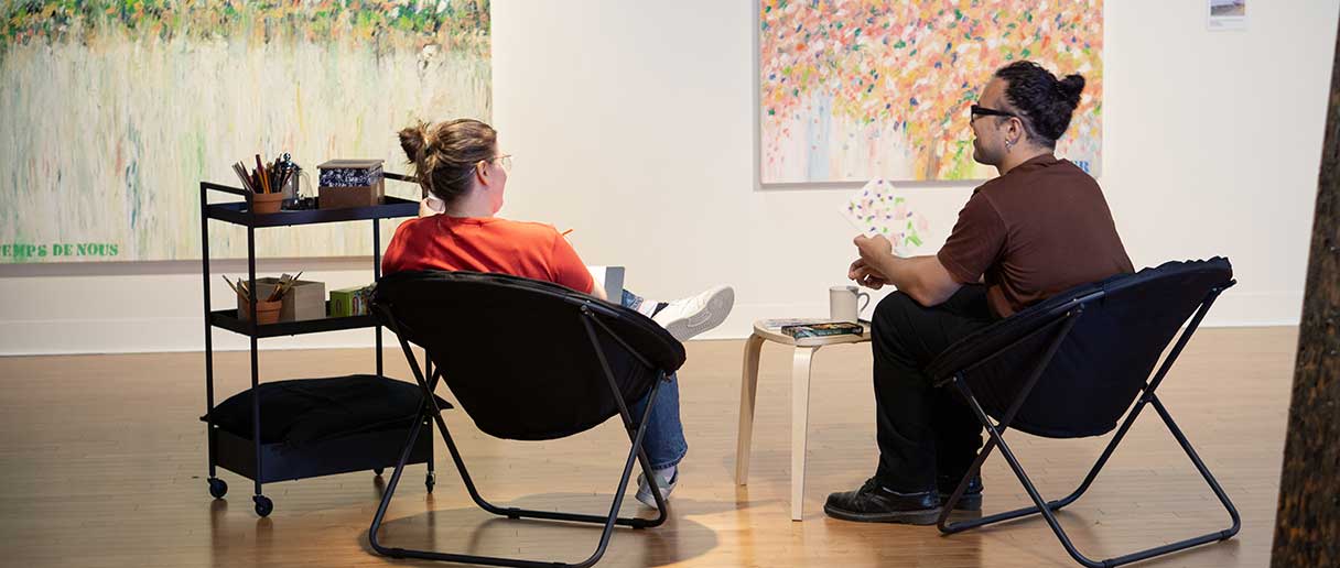 2 personnes assises discutent en regardant des toiles sur le mur