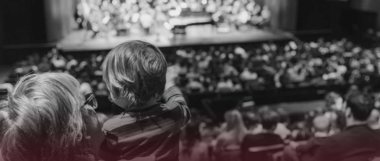 Un enfant dans les bras de sa mère regarde la scène.