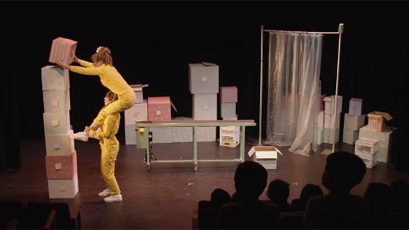 1 femme sur les épaules d'une autre femme empilant des boites pour former une tour.