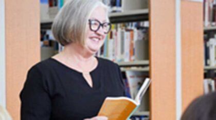 Une dame debout dans une bibliothèque avec un livre dans ses mains