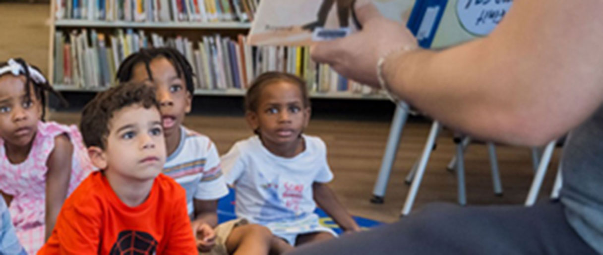 Des enfants assis regardant un livre tendu par une personne adulte lors de l'heure du conte inclusive