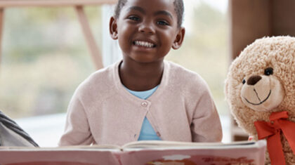 Une enfant et un nounours devant un livre de lecture