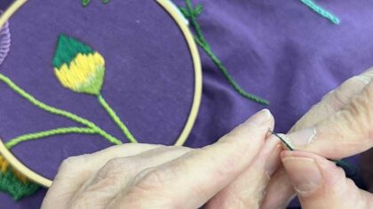 Main avec une aiguille qui brode une fleur sur un tissu mauve