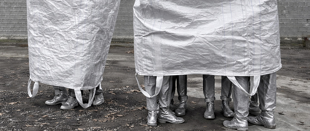Une œuvre de Giorgia Volpe, intitulée Monumental Togetherness (2026) : photo de gens recouverts d'un sac de plastique géant. Ouevre réalisée à partir de matériaux récupérés (tissus, sacs de plastique, objets domestiques).