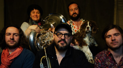 Fanfare sous le pommier | Le trompettiste et compositeur Jacques Kuba Séguin à l'avant-plan, au centre, accompagné de d'autres musiciens et d'un chien,