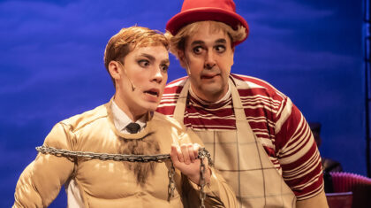 Spectacle Mon père se prend pour Fellini — Deux interprètes se tiennent au premier plan : l’un porte une chaîne sur le torse, l’autre, coiffé d’un chapeau rouge, l’accompagne de près.