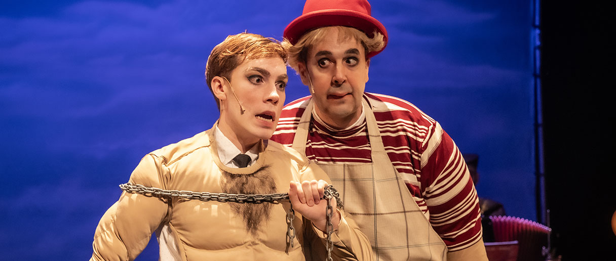 Spectacle Mon père se prend pour Fellini — Deux interprètes se tiennent au premier plan : l’un porte une chaîne sur le torse, l’autre, coiffé d’un chapeau rouge, l’accompagne de près.