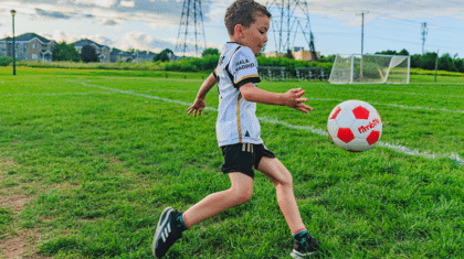 Un enfant de 7-8 ans avec un ballon de soccer sur un terrain extérieur