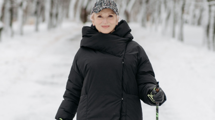 Une dame âgée marchant dans la neige avec des bâtons de marche